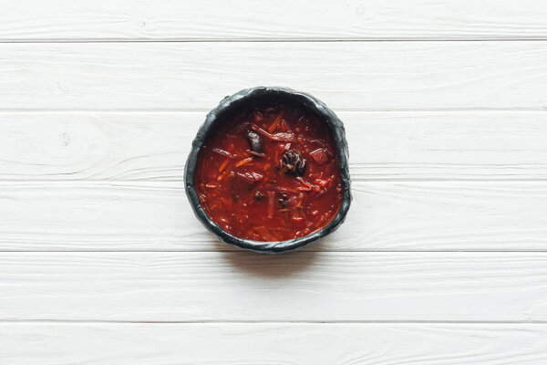 top view of traditional beetroot soup in bowl on white wooden background