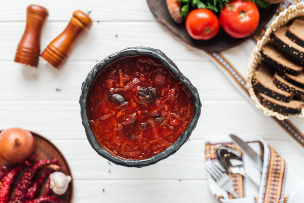 selective focus of tasty traditional beetroot soup with ingredients around on white wooden background