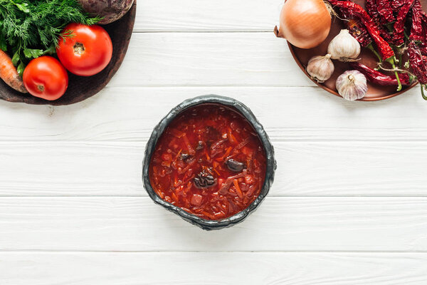 top view of traditional beetroot soup with vegetable ingredients on white wooden background