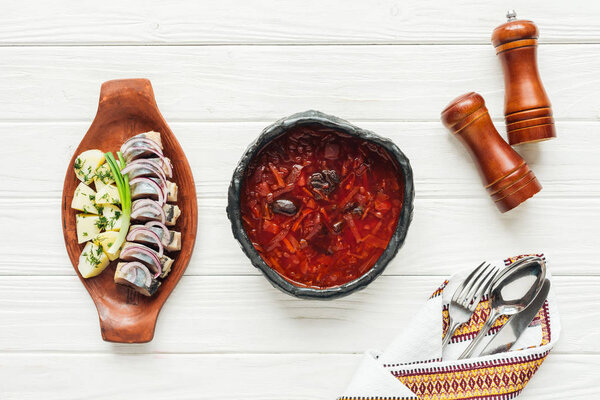 top view of traditional beetroot soup with herring and cutlery on white wooden background