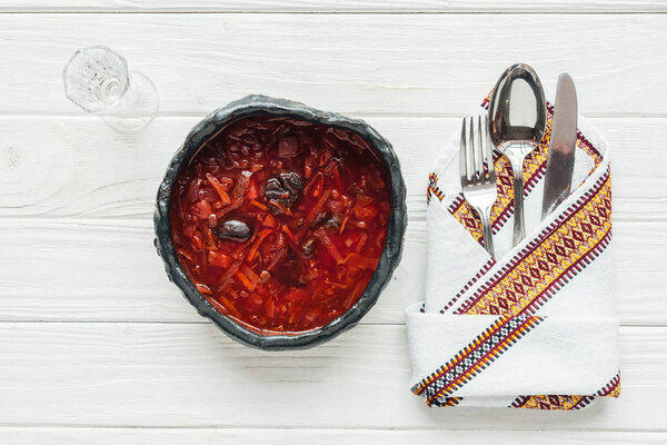 top view of traditional beetroot soup with cutlery and glass of vodka on white wooden background
