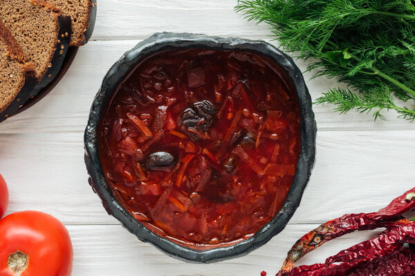 bowl of traditional beetroot soup with ingredients on white wooden background