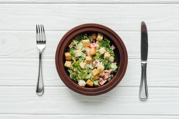 Top view of tasty traditional caesar salad with croutons in bowl and cutlery on white wooden background — Stock Image Top View Tasty Traditional Caesar Salad Croutons Bowl Cutlery White Stock Image