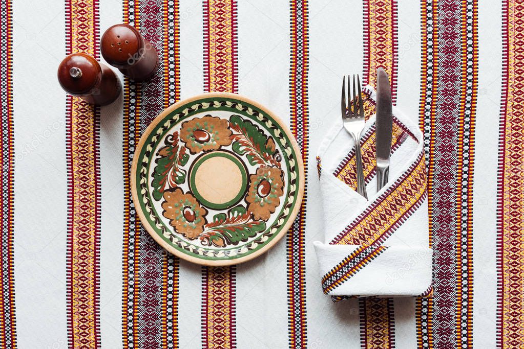 top view of traditional table setting with ornate plate on embroidered tablecloth