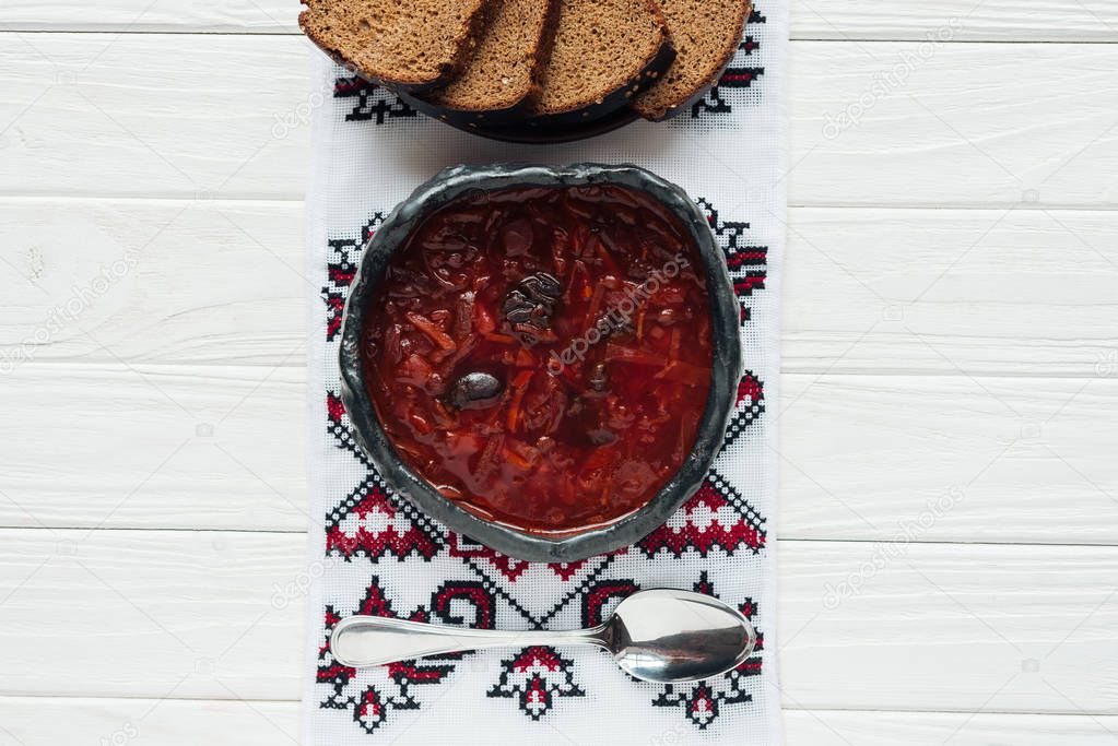 bowl of traditional beetroot soup with embroidered towel and rye bread on white wooden background