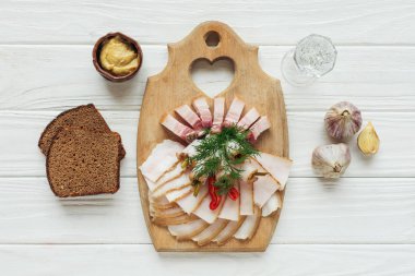 traditional sliced smoked lard on cutting board with mustard, glass of vodka and rye bread on white wooden background clipart