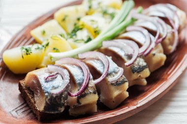 close up of tasty marinated herring with potatoes and onions in earthenware plate clipart