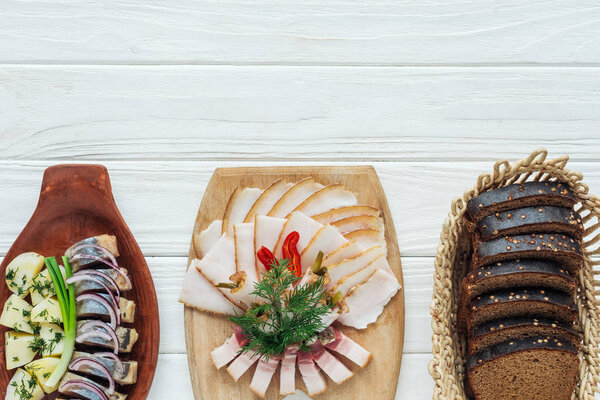 traditional sliced smoked lard on cutting board, rye bread and herring on white wooden background