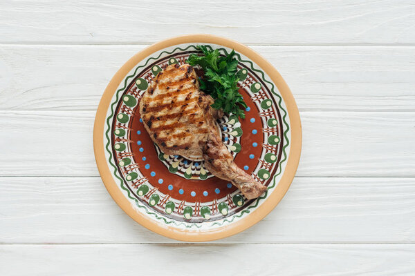 top view of grilled rib eye meat steak on plate with parsley on white wooden background