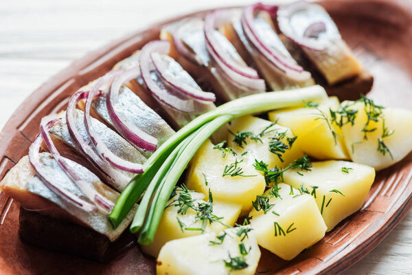 close up of delicious marinated herring with potatoes and onions in earthenware plate