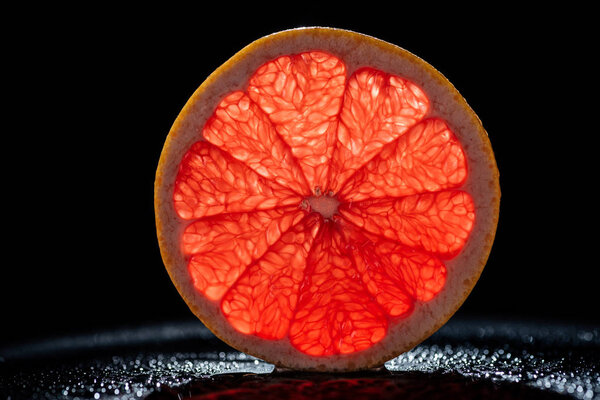 slice of grapefruit with red backlit on black background 