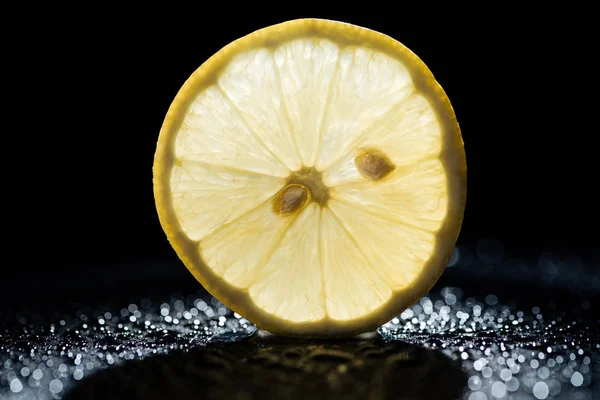 一片柠檬在黑色的背景与水滴和背光 — 图库照片