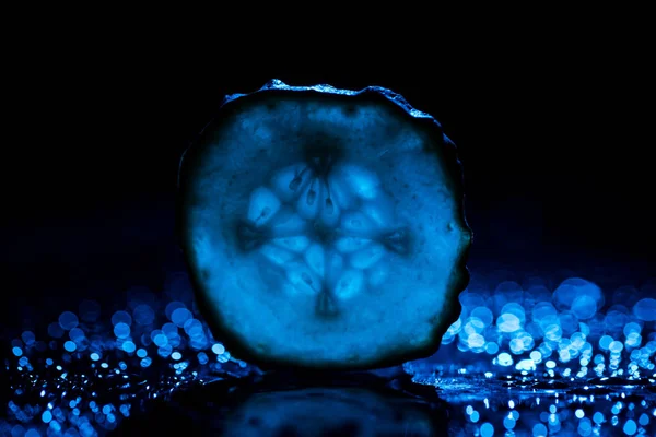 slice of cucumber with blue back light on black background