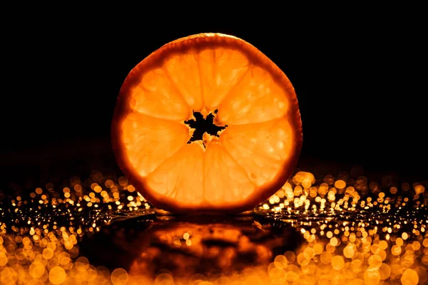 slice of orange on black background with bokeh and backlit