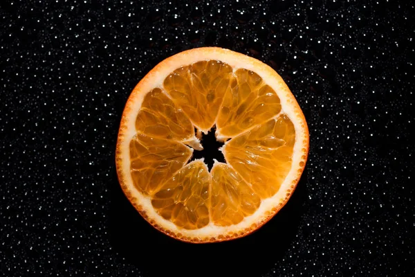 slice of orange on black background with water drops