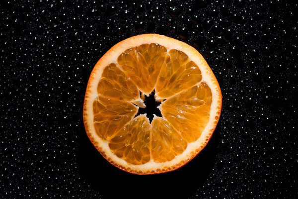 slice of orange on black background with water drops