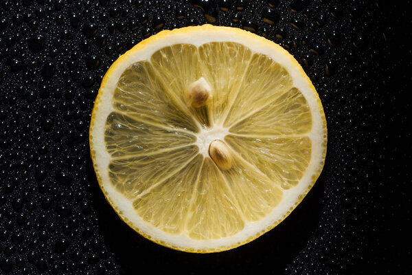 slice of fresh lemon on black background with water drops