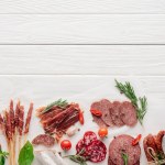 Flat lay with bottle of red wine, bottle opener and meat snacks on wooden surface