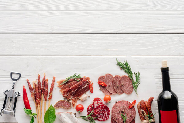 flat lay with bottle of red wine, bottle opener and meat snacks on wooden surface
