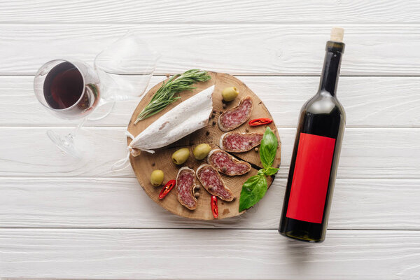 top view of bottle and glass of red wine with assorted meat appetizers on white wooden surface