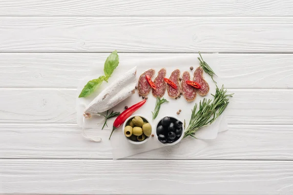 在白色木制桌面上可以看到橄榄 迷迭香和罗勒叶的肉类开胃菜的顶视图 — 图库照片