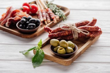 food composition with various meat appetizers, olives and basil leaves on white wooden surface clipart