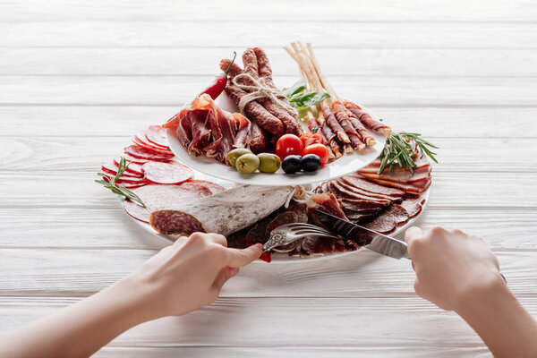 cropped shot of woman trying different meat appetizers at white wooden surface