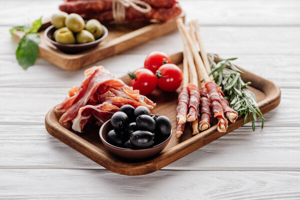 food composition with various meat appetizers, olives and rosemary on white wooden surface