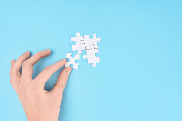 partial view of woman with white puzzles pieces on blue background