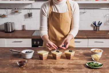 orta bölümde üçlü çikolata mousse bardaklarda hazırlanıyor önlük içinde kadın