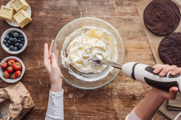 partial top view of woman mixing cream for delicious homemade cake