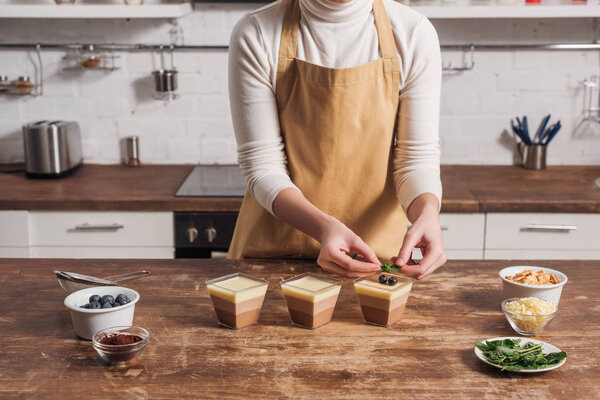 mid section of woman in apron preparing triple chocolate mousse dessert with blueberries 