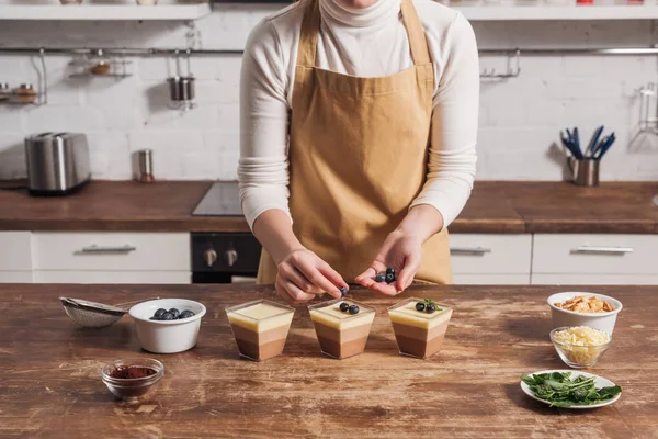 orta bölümde üçlü çikolata mousse bardaklarda hazırlanıyor önlük içinde kadın