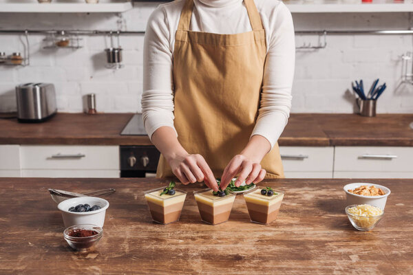 cropped shot of woman in apron preparing triple chocolate mousse in glasses