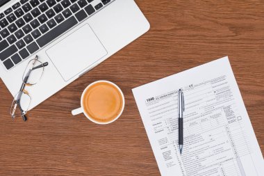 Masa üzerinde vergi formu, laptop, yapışkan notlar ve kahve üstten görünüm
