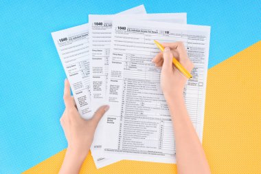 partial view of woman filling tax forms on blue and yellow background clipart