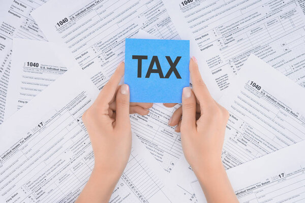 cropped view of woman holding blue card with word 'tax' and documents on background 