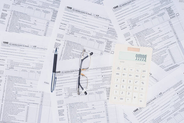 top view of calculator, pen and glasses with tax forms on background
