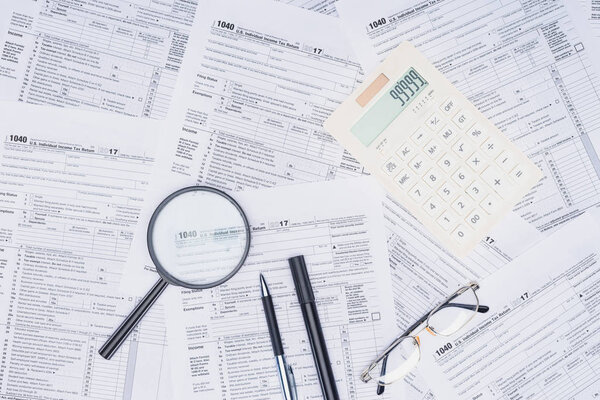 top view of calculator, magnifying glass and stationery with tax forms on background