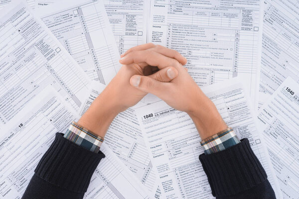 cropped view of man with folded hands on background with tax forms