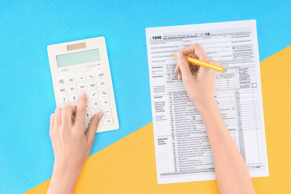 обрезанный вид женщины с помощью калькулятора и заполнение налоговой формы на синем и желтом фоне
