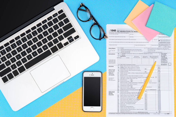 top view of tax form and digital devices on blue and yellow background