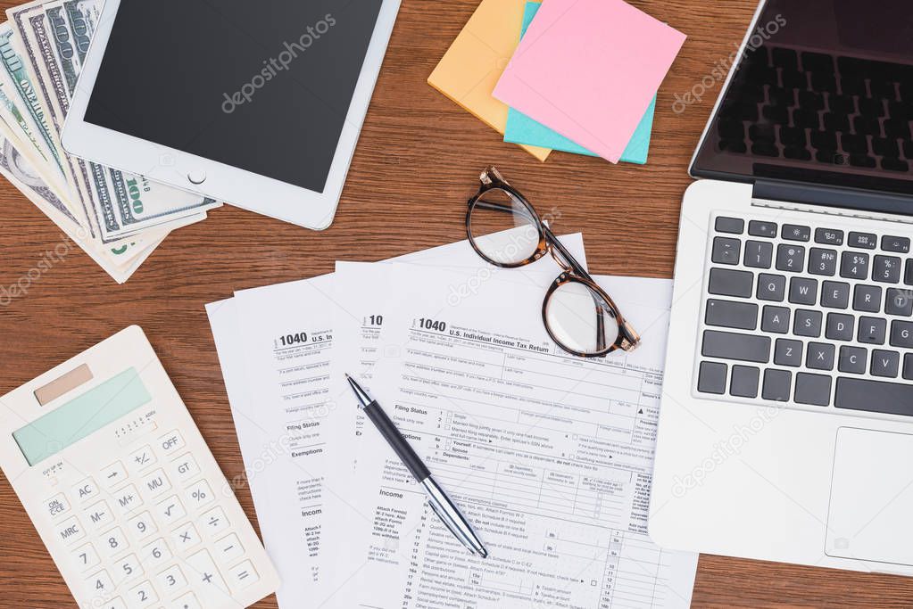 top view of tax forms, digital devices and stationery on desk