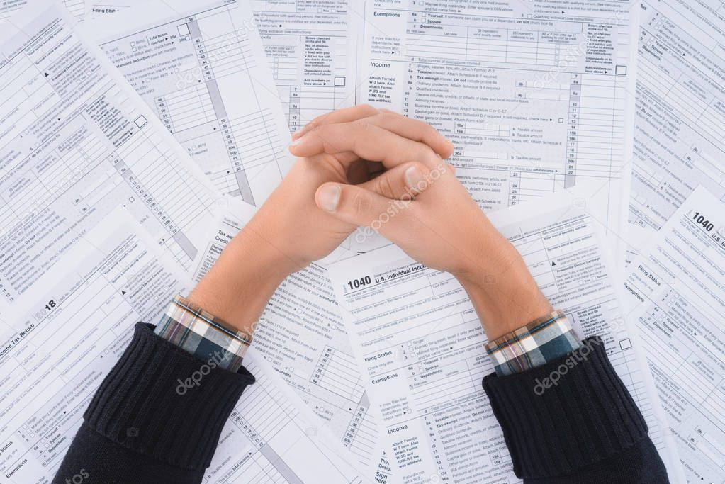 cropped view of man with folded hands on background with tax forms