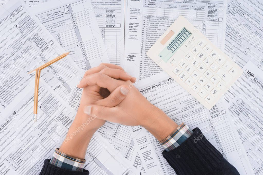 cropped view of man with folded hands, broken pencil and calculator with tax forms on background