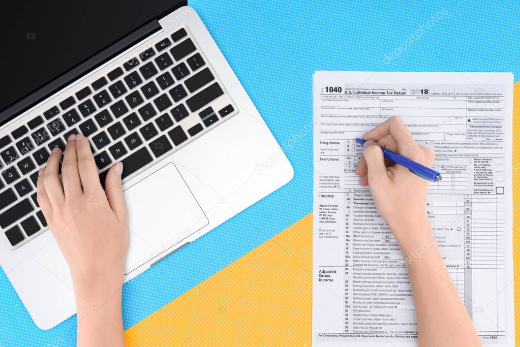 cropped view of woman typing on laptop and filling tax form on blue and yellow background