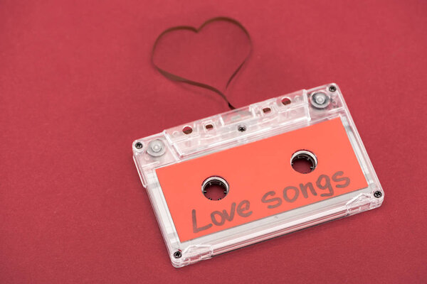 close up view of audio cassette with lettering love songs and heart symbol made of tape isolated on red, st valentine day concept