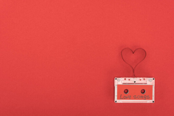 elevated view of audio cassette with lettering love songs and heart symbol made of tape isolated on red, st valentine day concept