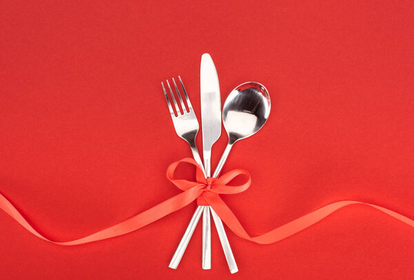 flat lay with fork, knife and spoon wrapped by red festive ribbon isolated on red, st valentine day concept