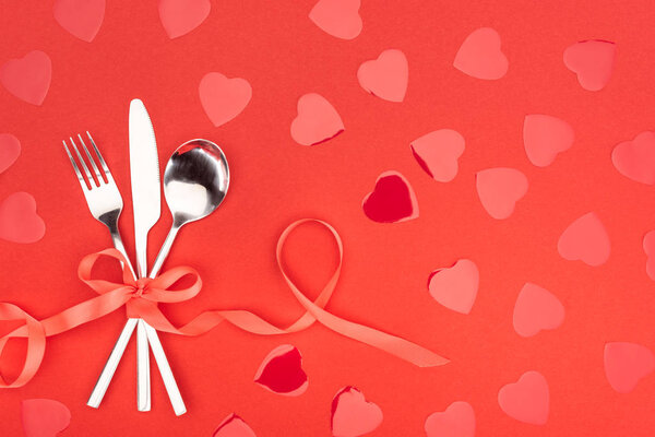 Плоский лежал со столовыми приборами, обернутыми праздничной лентой рядом с символами сердца изолированы на красный, День святого Валентина концепции
